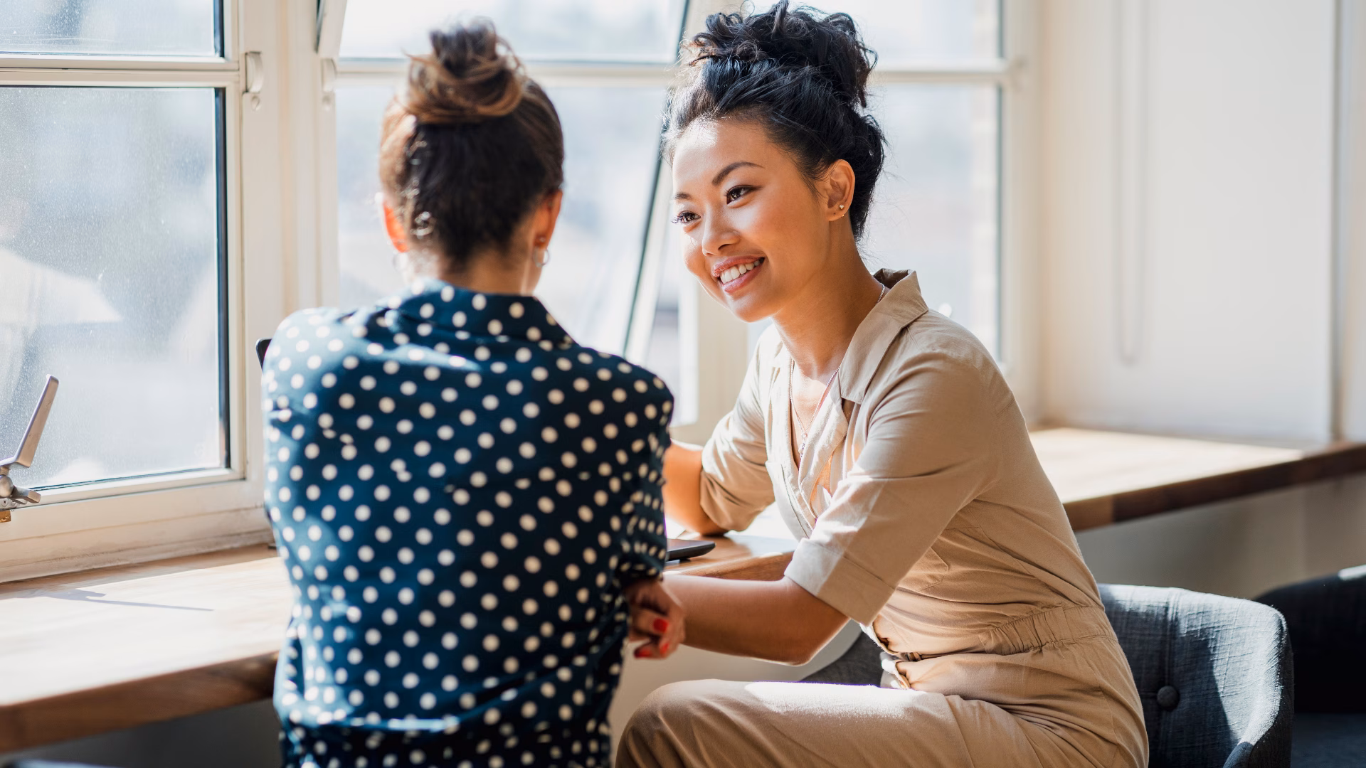 Two ladies talking in front of a window with a laptop.