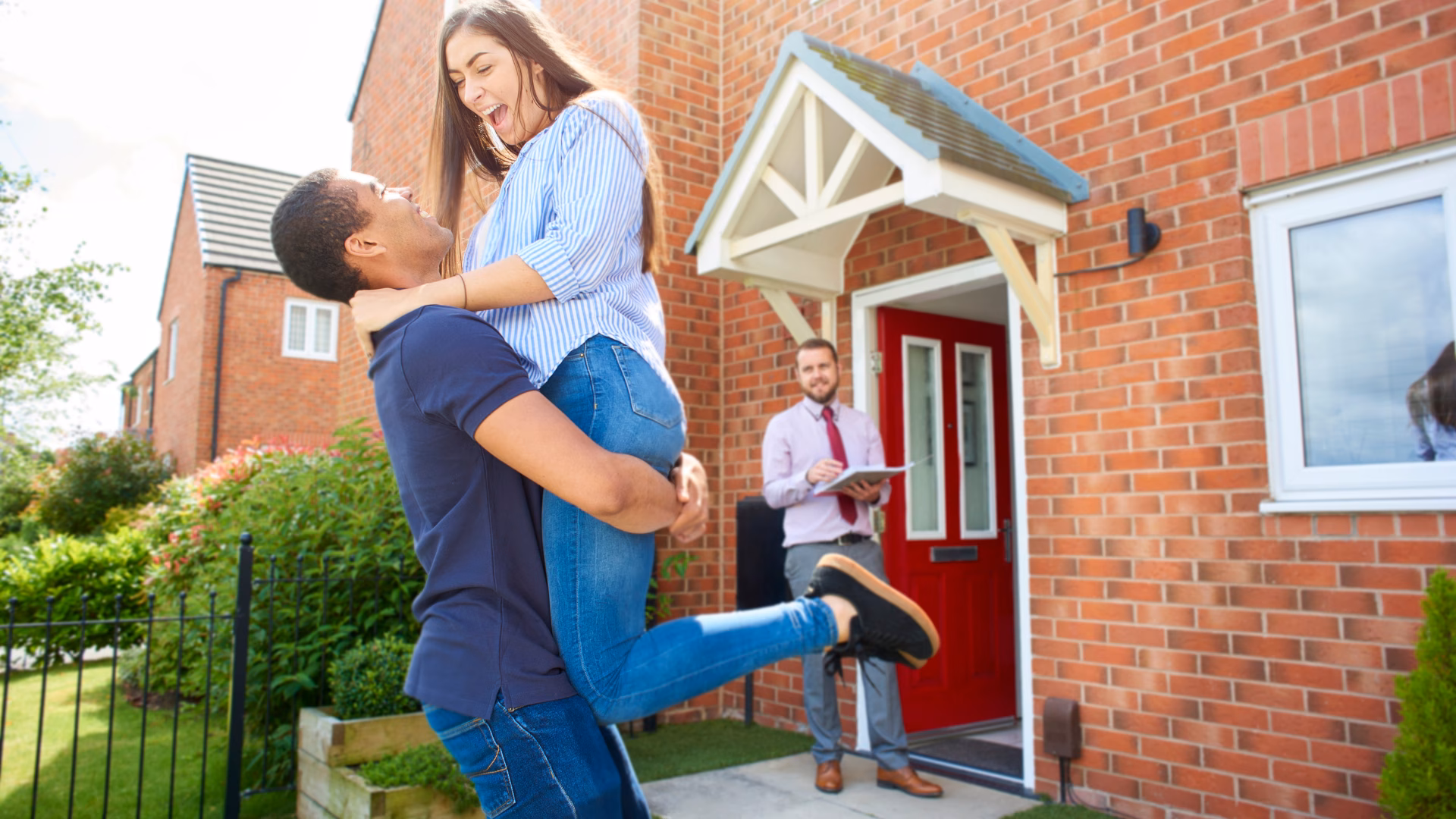 A man holding his wife in front of their new home.